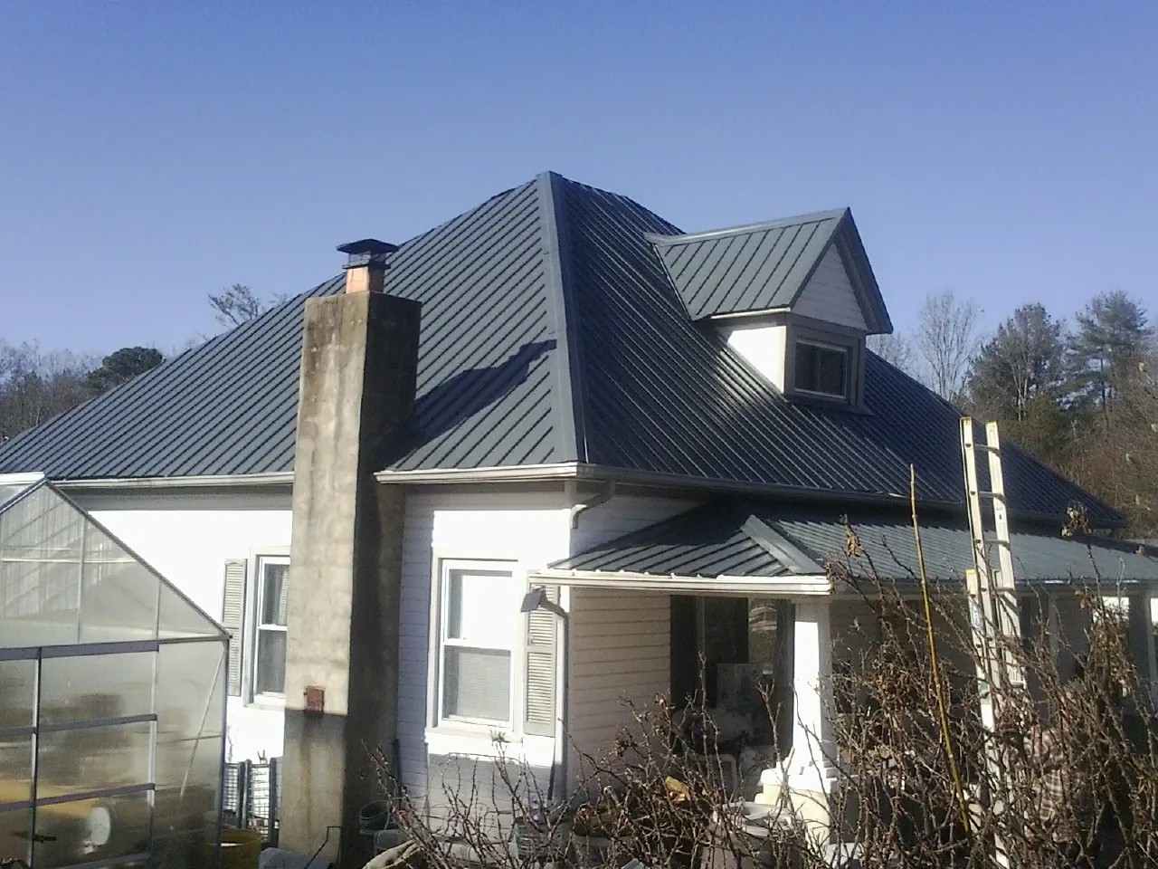 Dark blue standing seam metal roof on a white farmhouse with dormer — Slate & Tile Roof Repair by Roofing Brothers in Bonaire