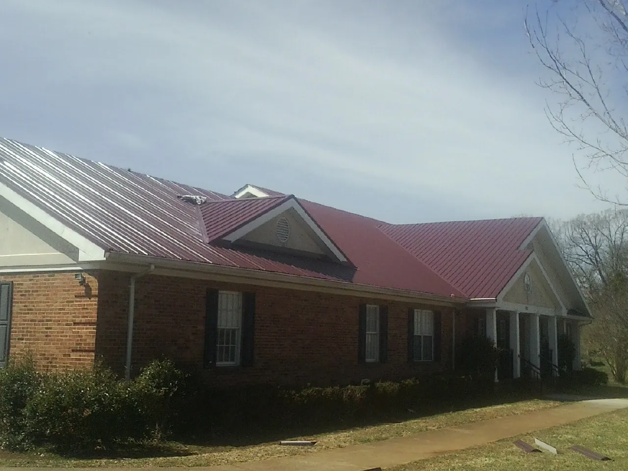 Red metal roof with gabled entries on a long brick building, from a Hail Damage Roof Repair job in Bonaire