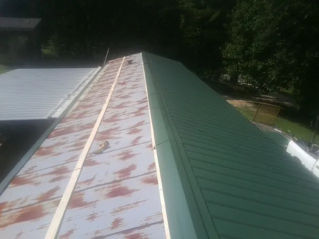 Old rusted panels beside newly installed green metal roofing — Wind Damage Roof Repair by Roofing Brothers in Bonaire