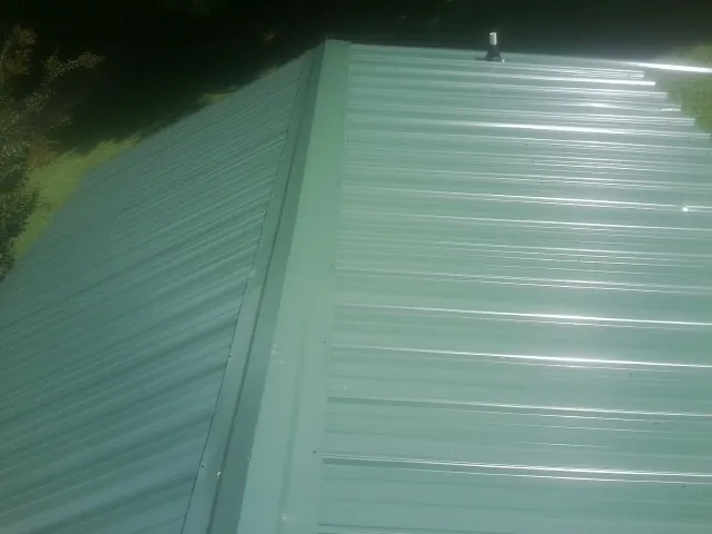 New green metal panels meeting at the ridge of a roof — Flat Roof Repair work by our crew in Bonaire