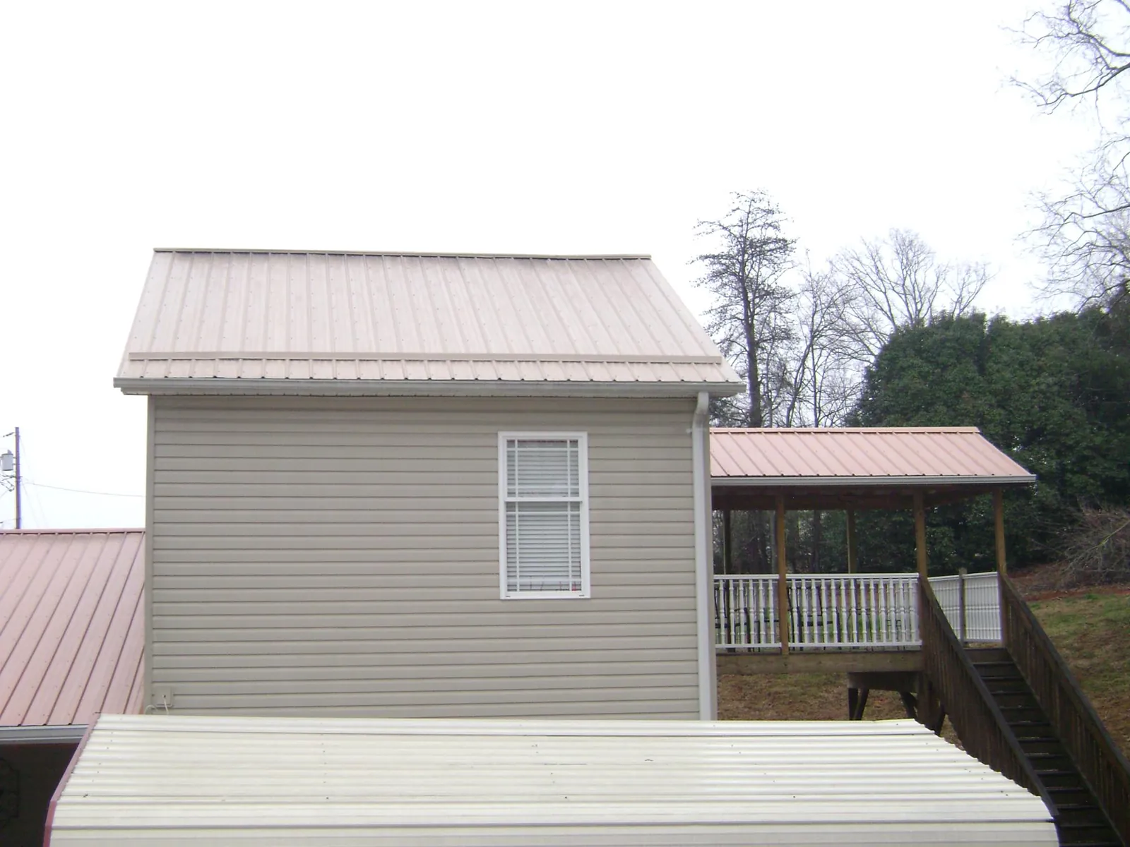 Tan metal roofs on a two story addition and attached porch, from a Roof Replacement job in Bonaire